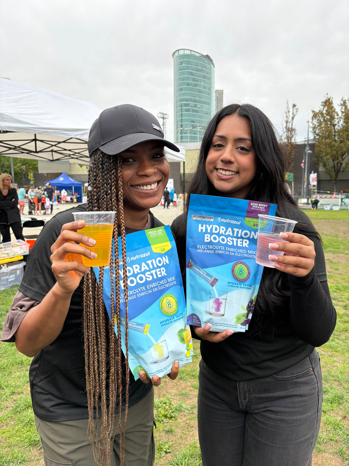 Two people holding Nutrazul Hydration Booster pouches and cups at RunSurreyRun 2025