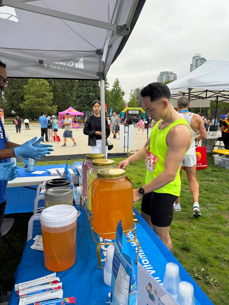 A runner filling a cup at the Nutrazul hydration table near the RunSurreyRun finish